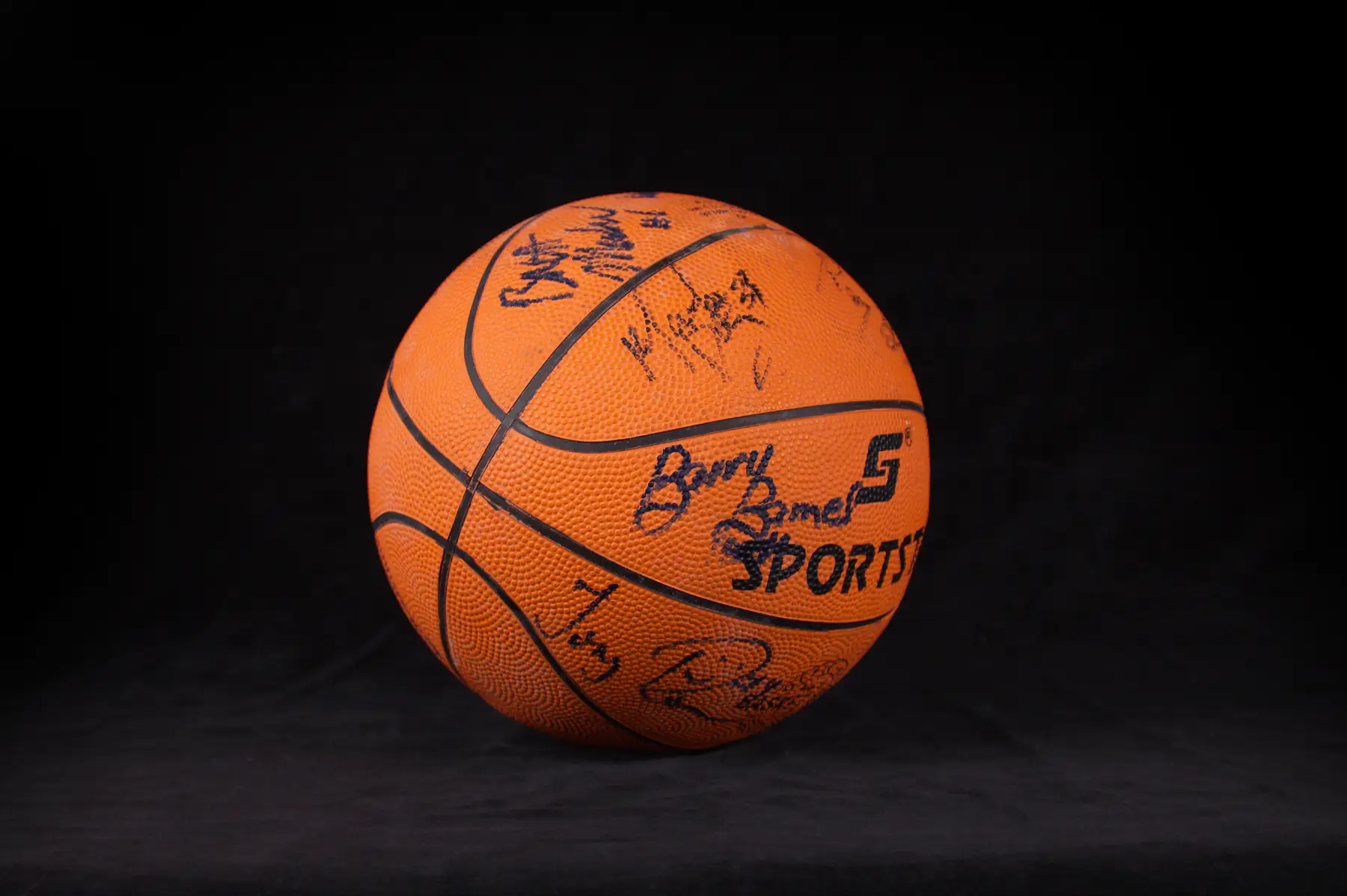 An orange Barry Barnes Sports basketball signed in black marker across several panels, photographed against black